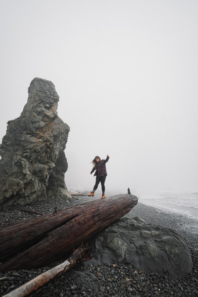 白天，穿着黑色夹克和黑色裤子的女人站在棕色岩石地层上